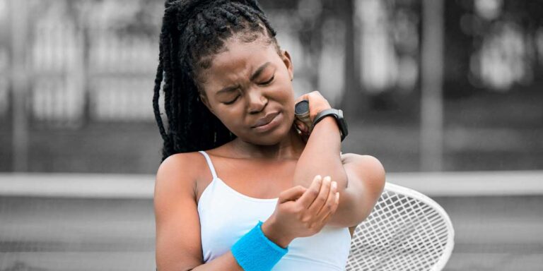 A Black woman grabbing her elbow and making a grimaced face, used to describe sports injuries