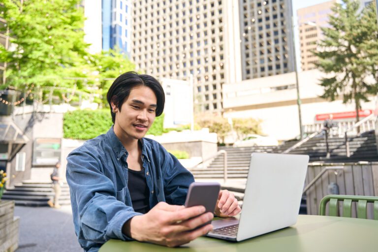 Young man smiling looking at phone and laptop.