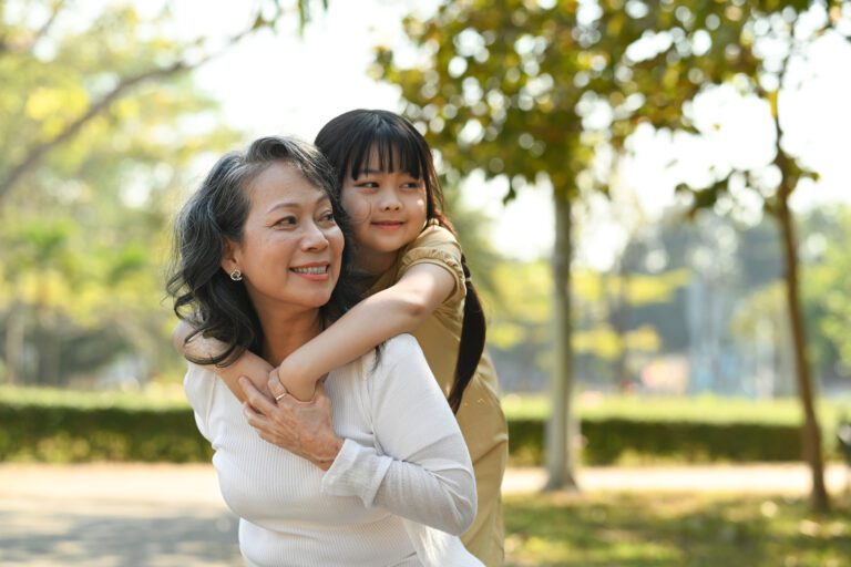 Image of smiling grandmother giving piggyback ride to cute little granddaughter during walking on in the park. Spine health