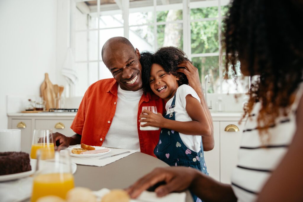 Father hugging and laughing with his family at the breakfast table