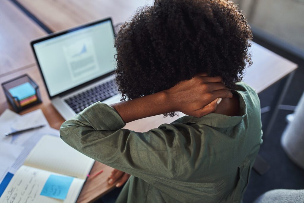 Elevated view of young woman holding neck pain looking at laptop documents